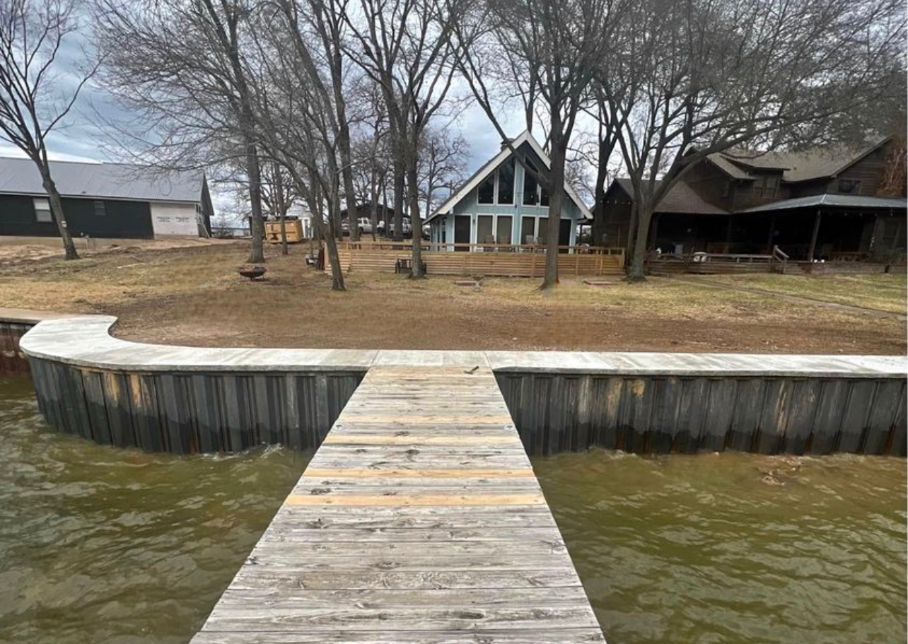 A wooden dock leading to a house on a lake.