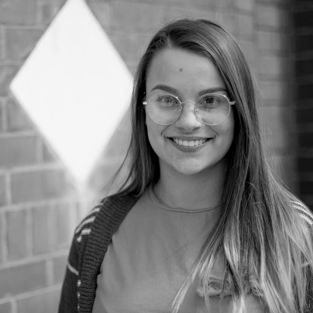 A woman wearing glasses is smiling in a black and white photo.