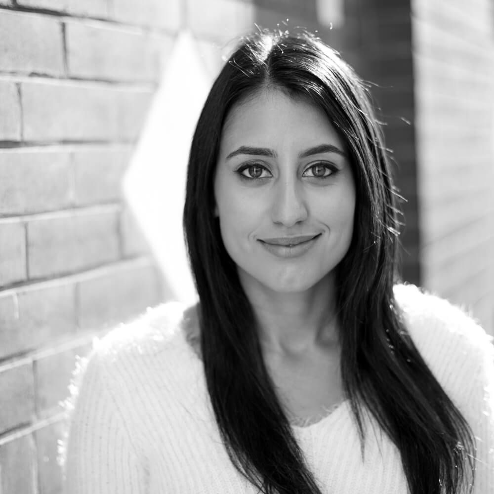 A black and white photo of a woman standing in front of a brick wall.