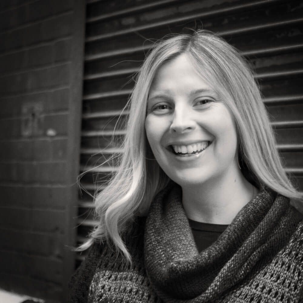 A woman wearing a sweater and scarf is smiling in a black and white photo.