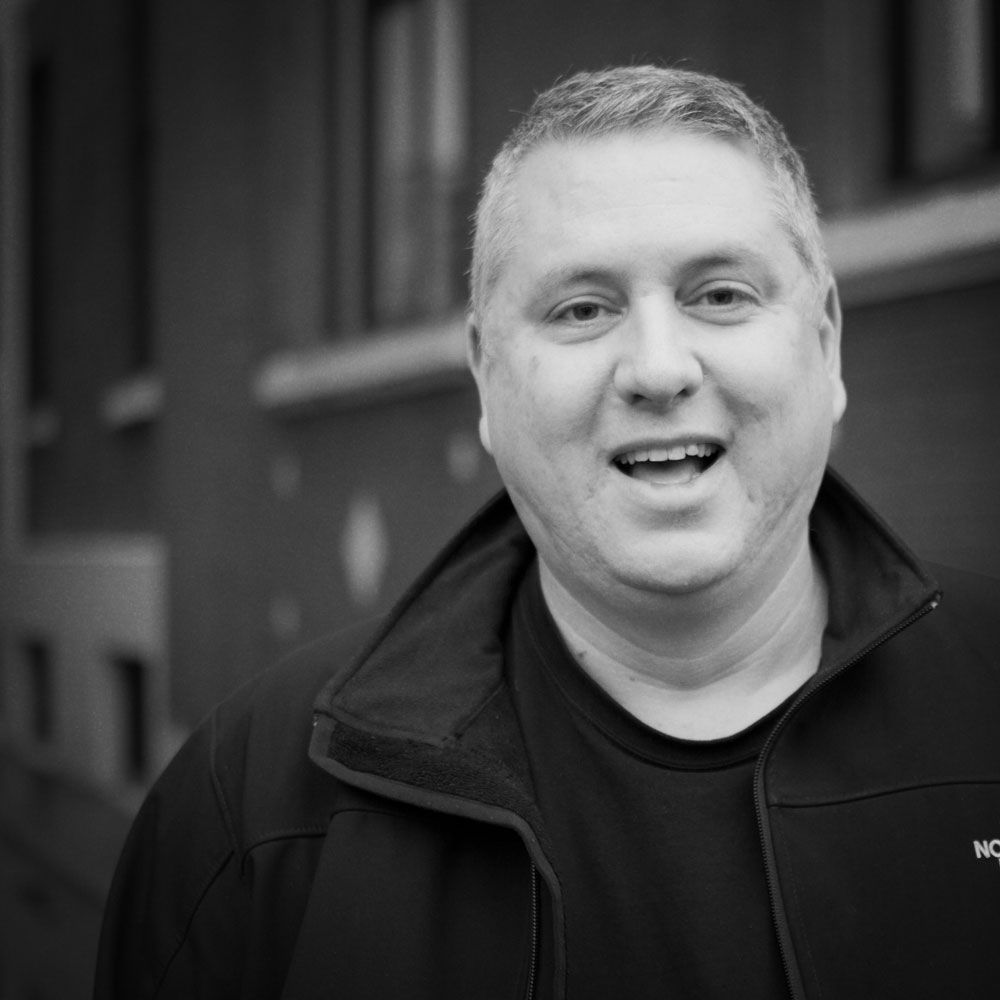 A man in a black jacket is smiling in a black and white photo.