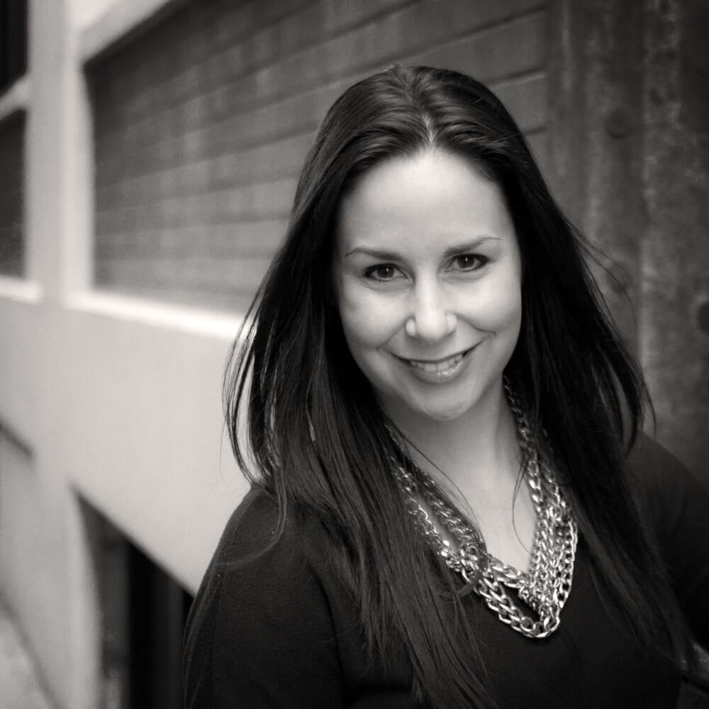 A black and white photo of a woman wearing a necklace and smiling.