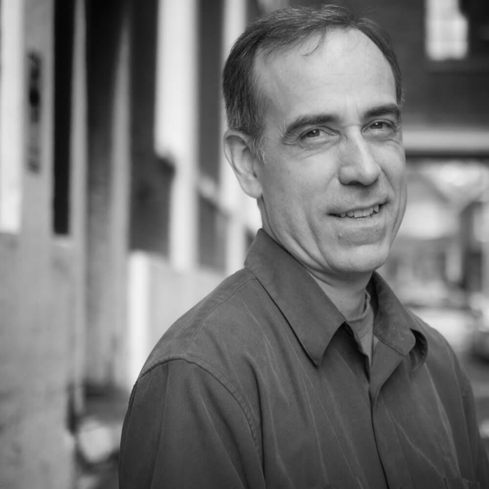 A man in a blue shirt is smiling in a black and white photo.