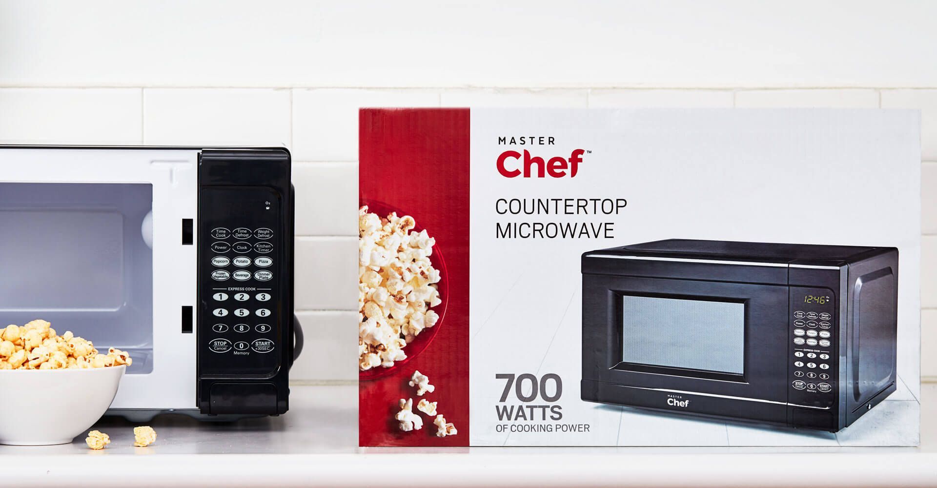 A chef countertop microwave is sitting on a counter next to a bowl of popcorn.