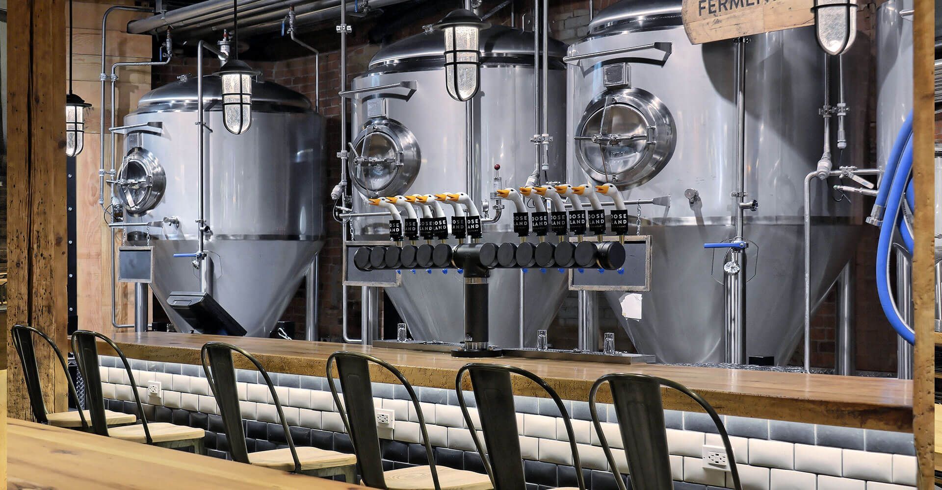 A bar in a brewery with a lot of tanks in the background.