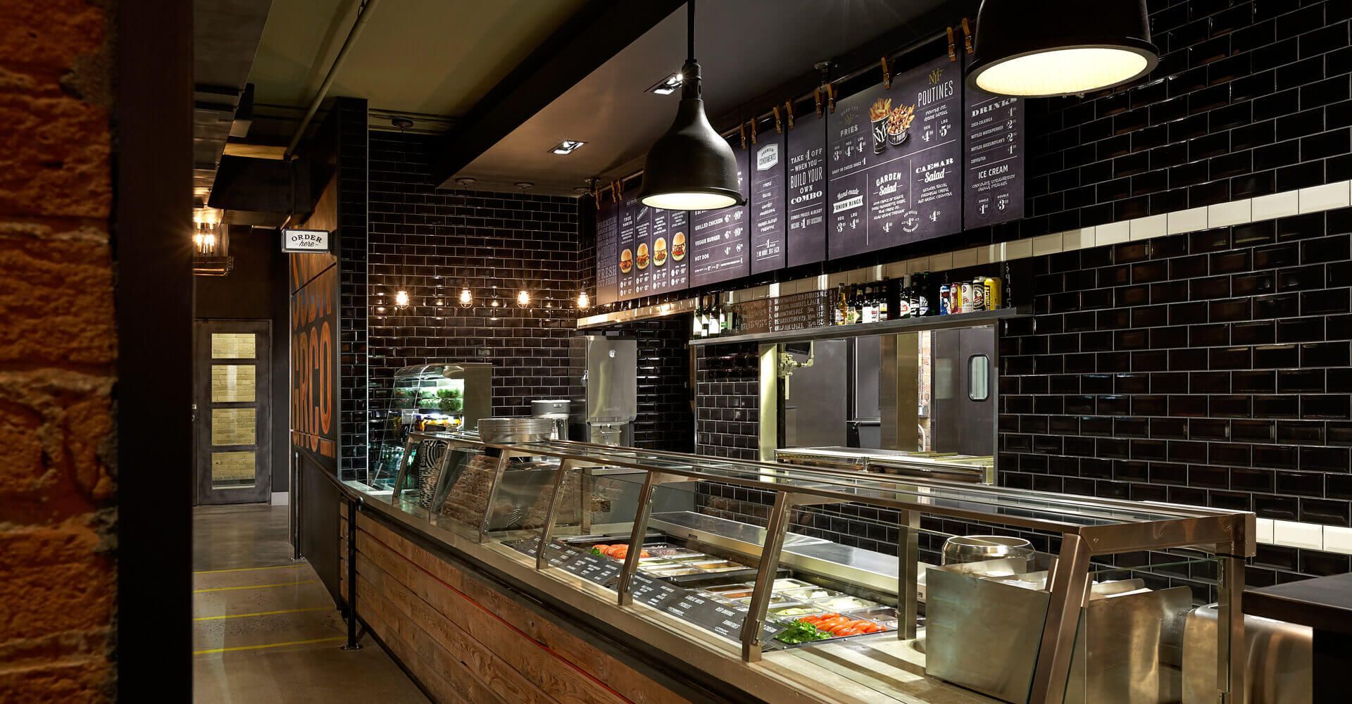 A long buffet line in a restaurant with black tiles and a brick wall.