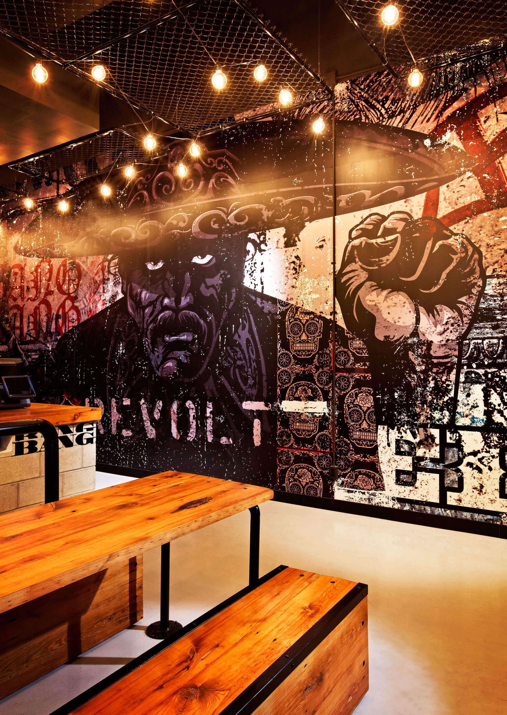 A room with a wooden table and benches and a large mural on the wall.