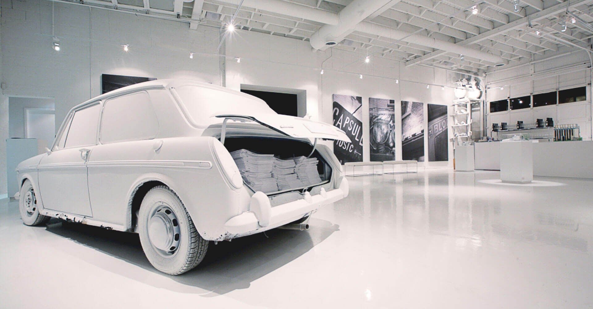 A white car is sitting in a white room with its trunk open.