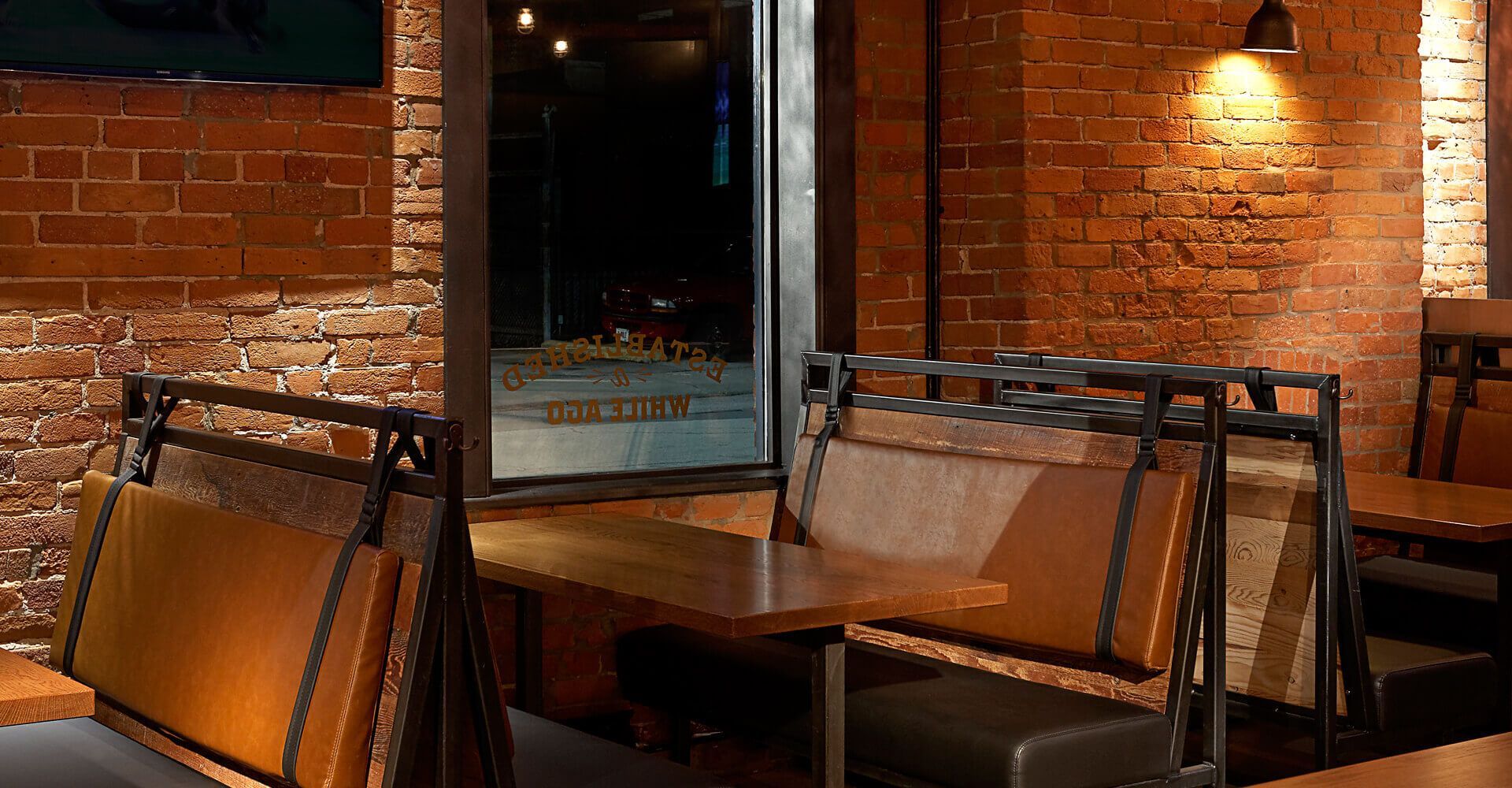 A restaurant with tables and benches and a brick wall.