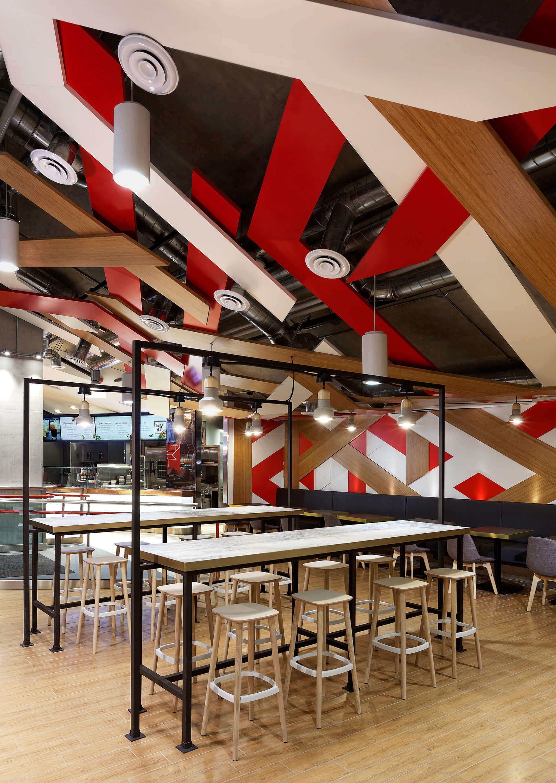 Empty modern café with bar stools, high tables, and bold red, white, and black geometric ceiling panels