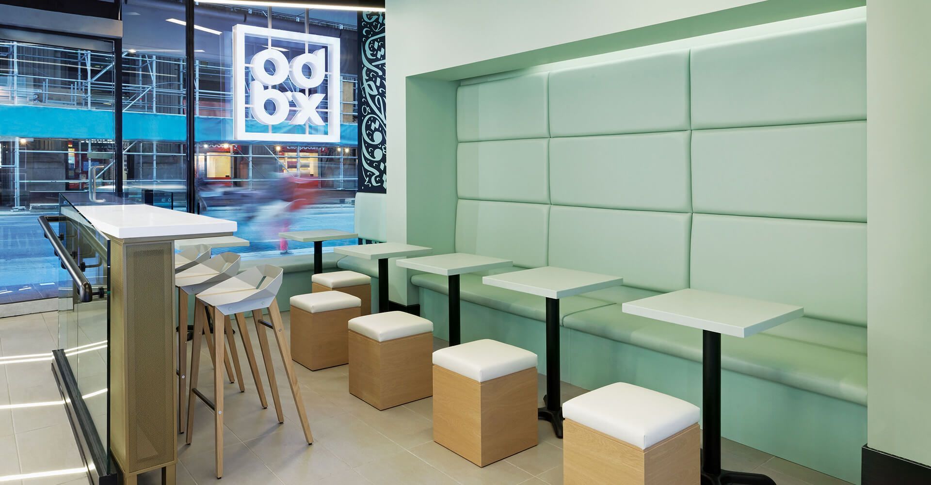 Modern lounge with mint-green benches, stools, and a high table by a window overlooking a city street