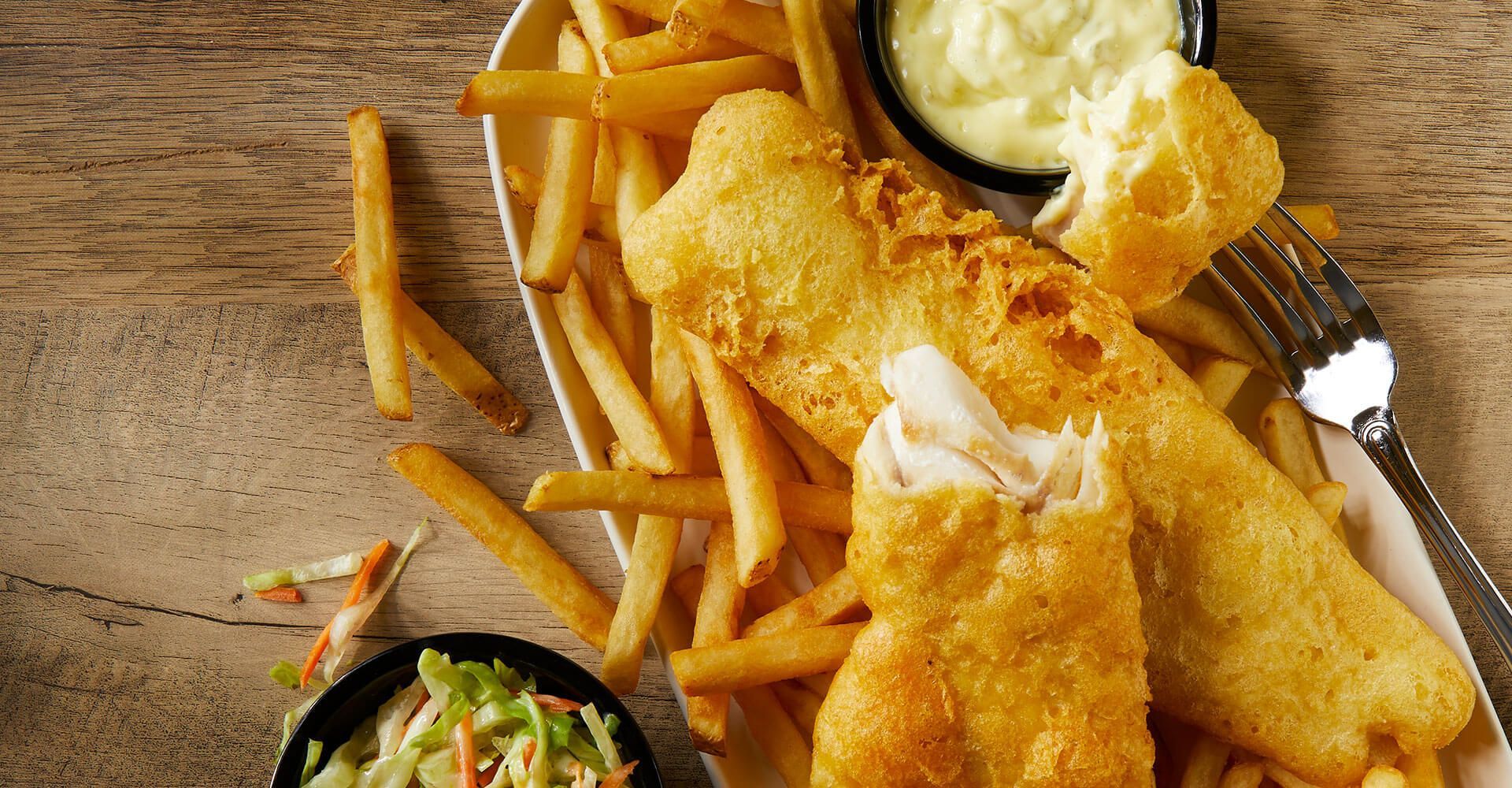 A plate of fish and french fries on a wooden table.