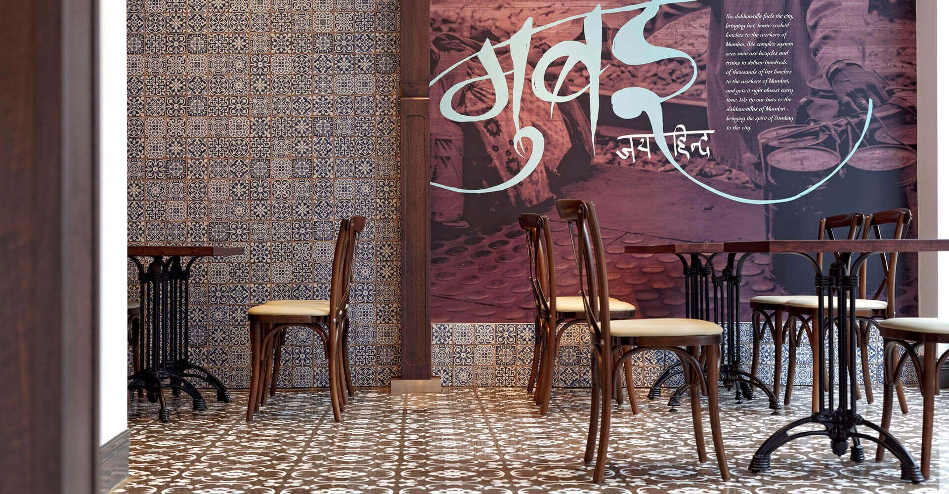 Empty café seating beside a brick wall with graffiti and mosaic tile flooring