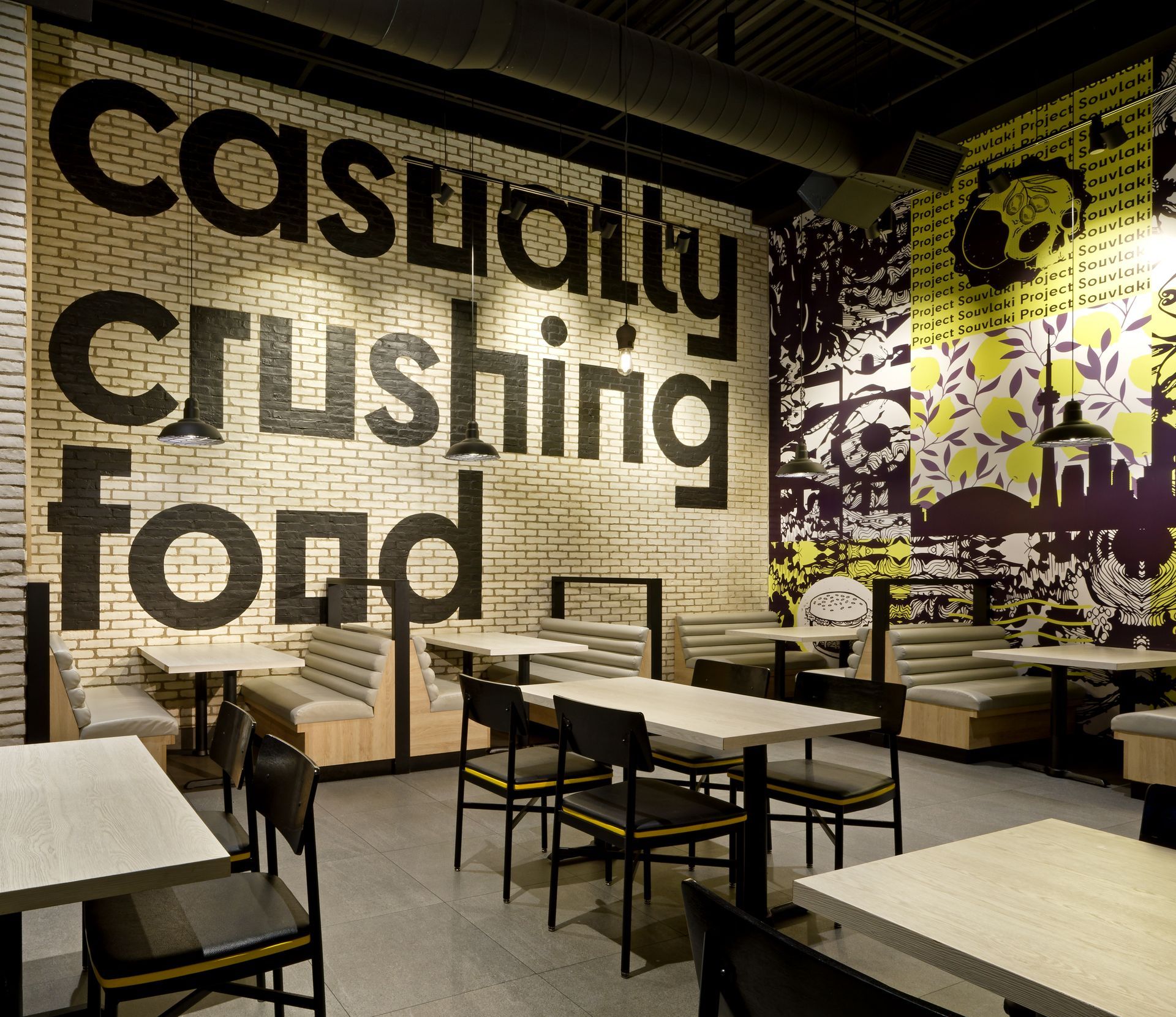 Restaurant interior with large black text mural reading “casually crushing food” on a yellow brick wall.