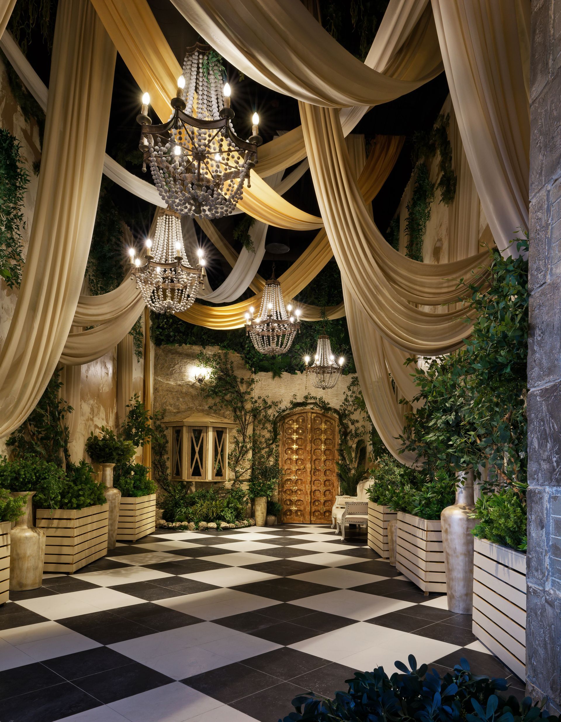 Elegant garden hallway with draped gold fabric, chandeliers, and a black-and-white checkered floor