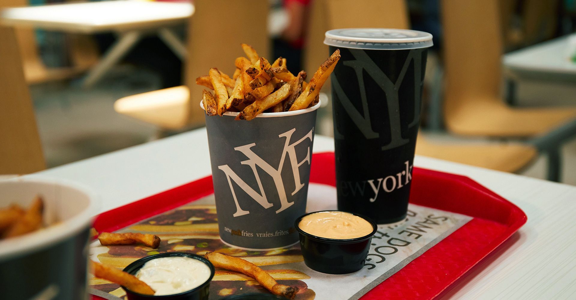 Fast-food tray with two black fries cups, dipping sauce, and fries on a red tray in a casual café.