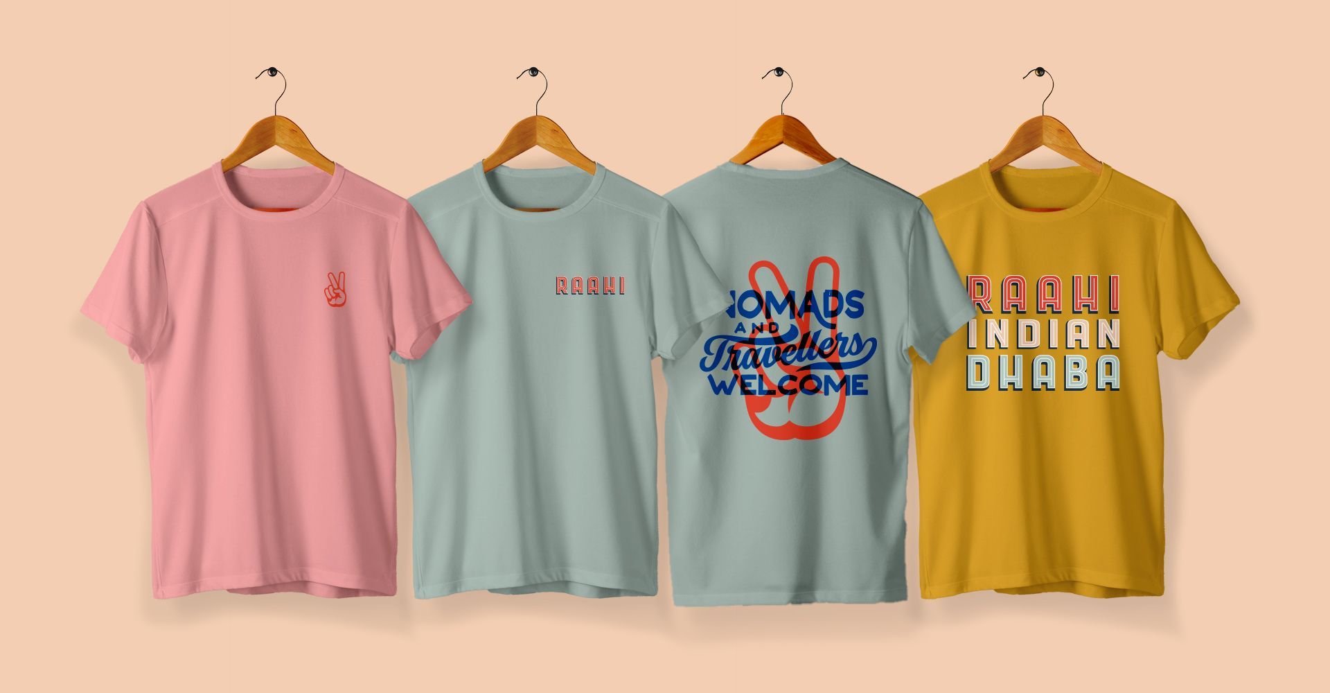 Four t-shirts are hanging on wooden hangers on a wall.