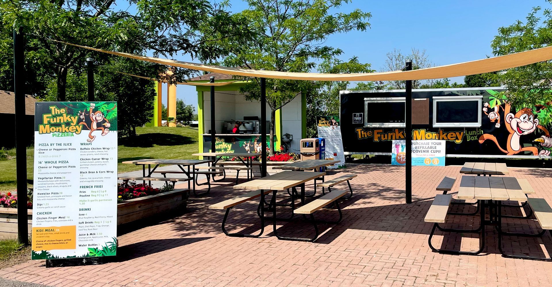 A food truck is parked in front of a picnic area with tables and benches.