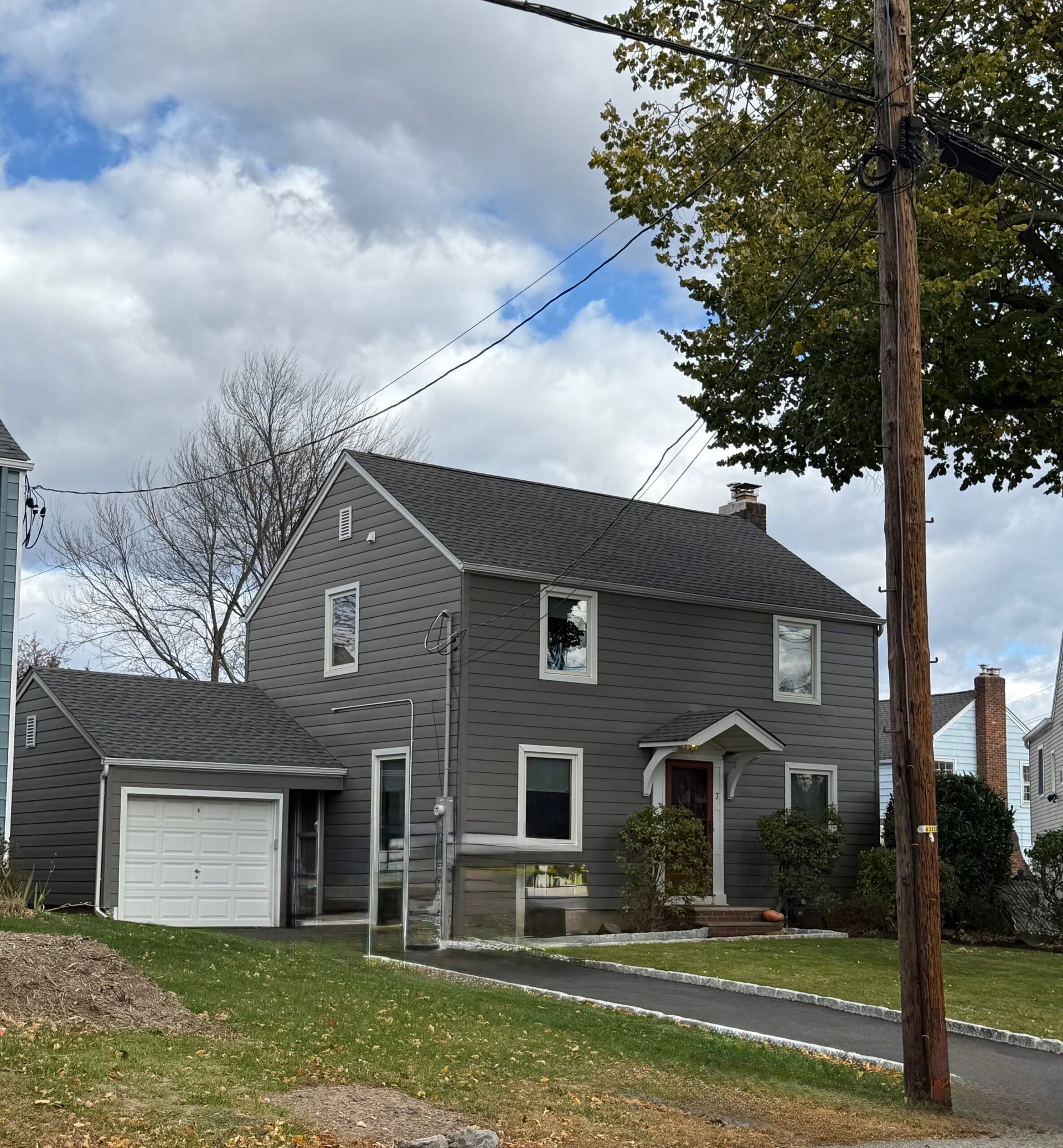 Gray two-story house with attached garage, dark roof, and driveway on a cloudy day.