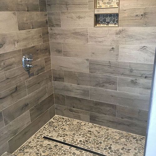 Shower stall with wood-look tile walls, pebble floor, and recessed shelf with mosaic tile.