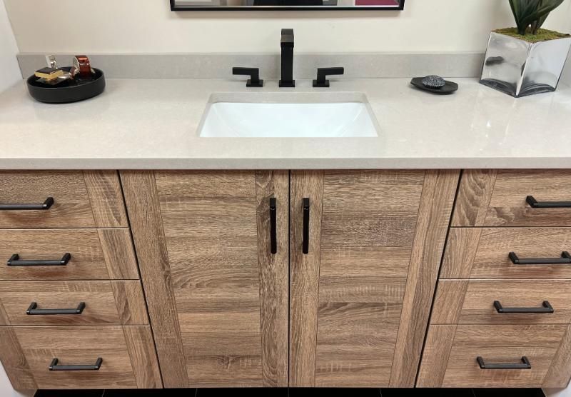 Bathroom vanity with light countertop, rectangular sink, black faucet, and brown wood cabinets.
