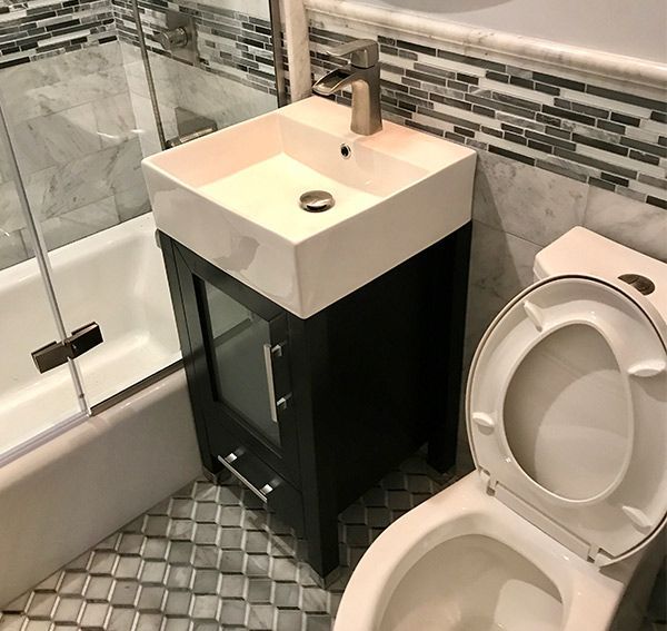 Bathroom with a small sink vanity, toilet, and bathtub with glass shower door.