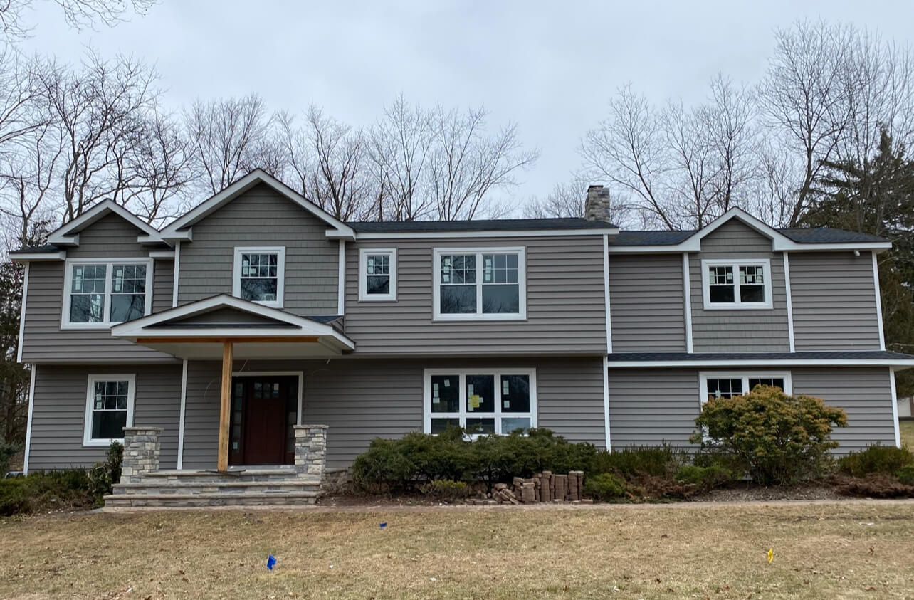 Gray house with multiple windows, wooden porch roof, and landscaping.
