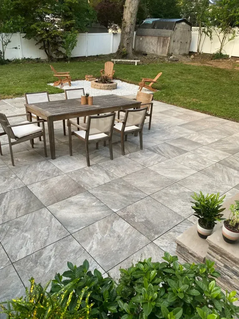 Patio with a large wooden table, chairs, fire pit, and shed in a backyard setting.