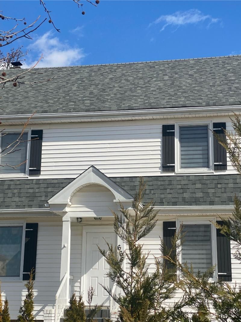 White house with gray roof and black shutters under a blue sky.