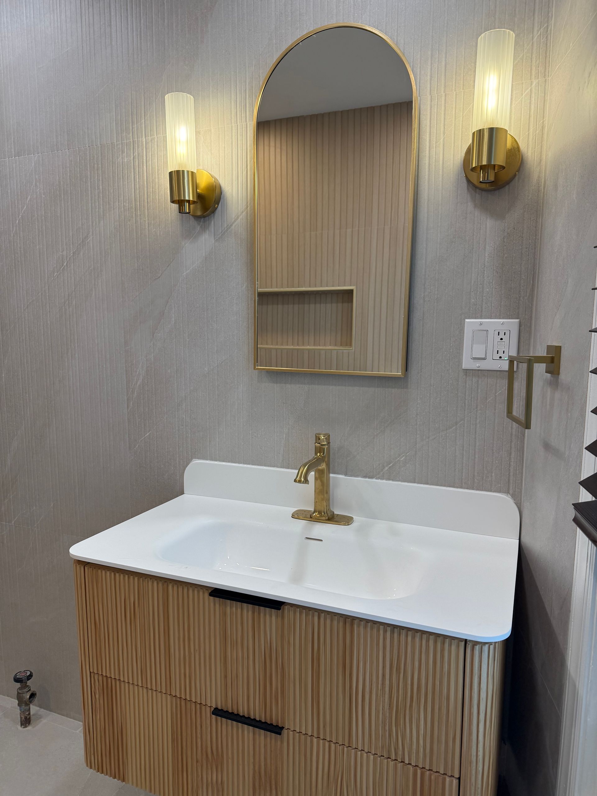 Modern bathroom vanity with arched mirror, gold sconces, and white sink on wood cabinet