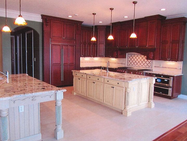 Spacious kitchen with dark wood cabinets, beige island, tiled counters, and hanging pendant lights create by American Home Remodeling