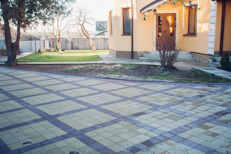 House entrance with tiled driveway and a small garden in warm evening light