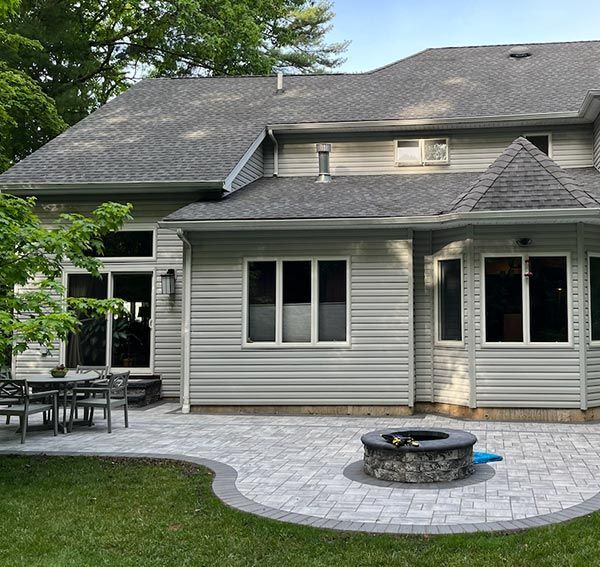 Backyard patio with gray brick, stone fire pit, and light gray house with windows.