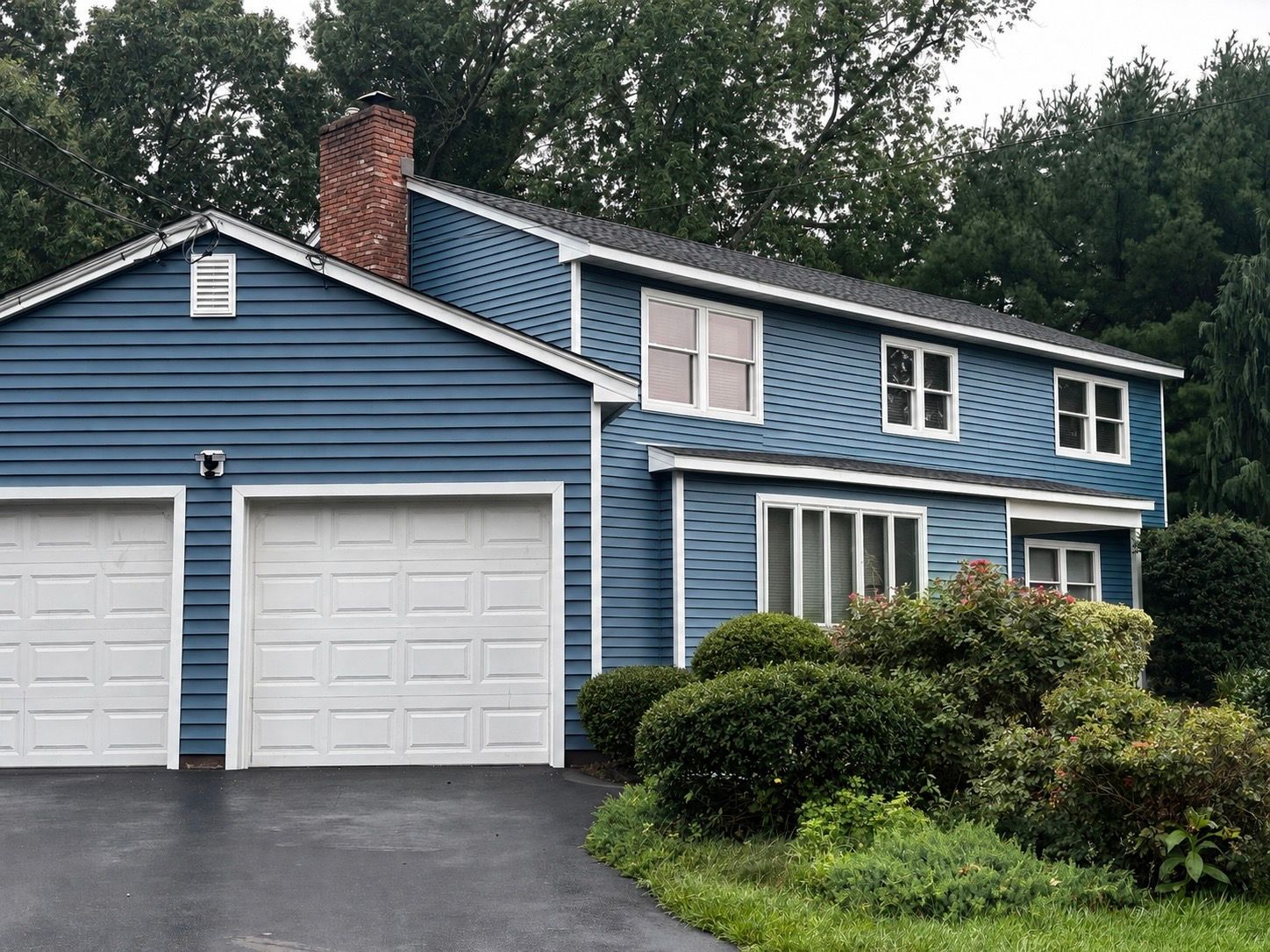 Blue two-story house with white garage doors and lush front landscaping