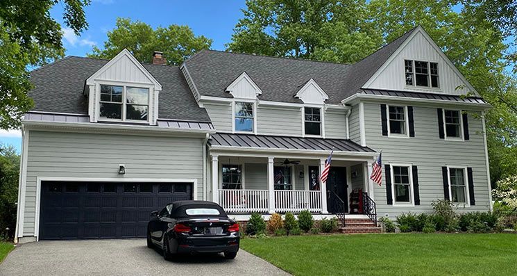 Two-story light green house with a dark gray roof and garage. A black car sits in the driveway.