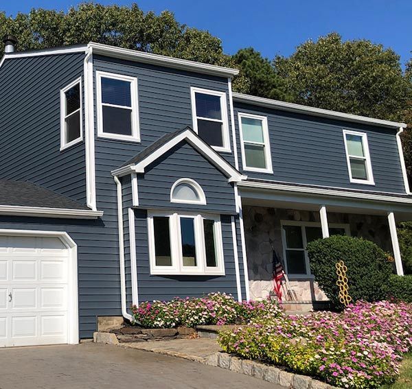 Two-story house with dark blue siding, white trim, and a stone facade. Flowers and garage in front.