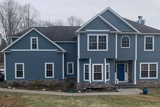 Two-story blue house with white trim, dark roof, stone base, and blue front door.
