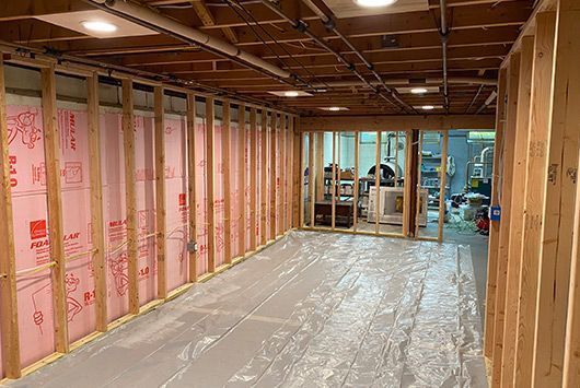 Basement renovation: Pink insulation between wood framing, plastic on floor.