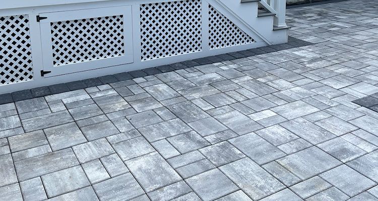 Gray paving stones under white latticework near steps.