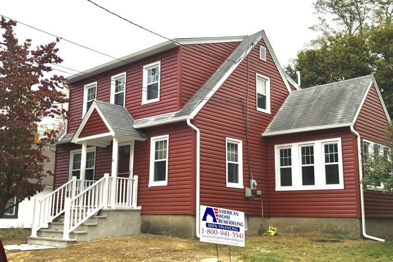 Red-sided two-story house with white trim, front porch, and sign on the lawn.