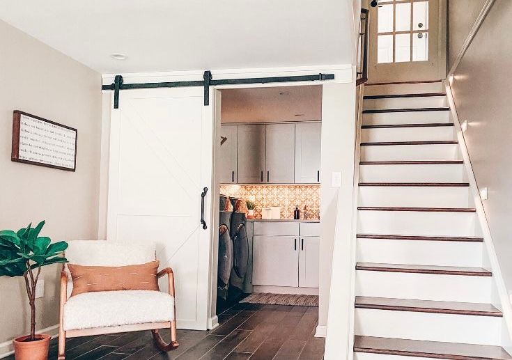 Barn door opens to kitchen with stairs on the right. A rocking chair sits near a potted plant.