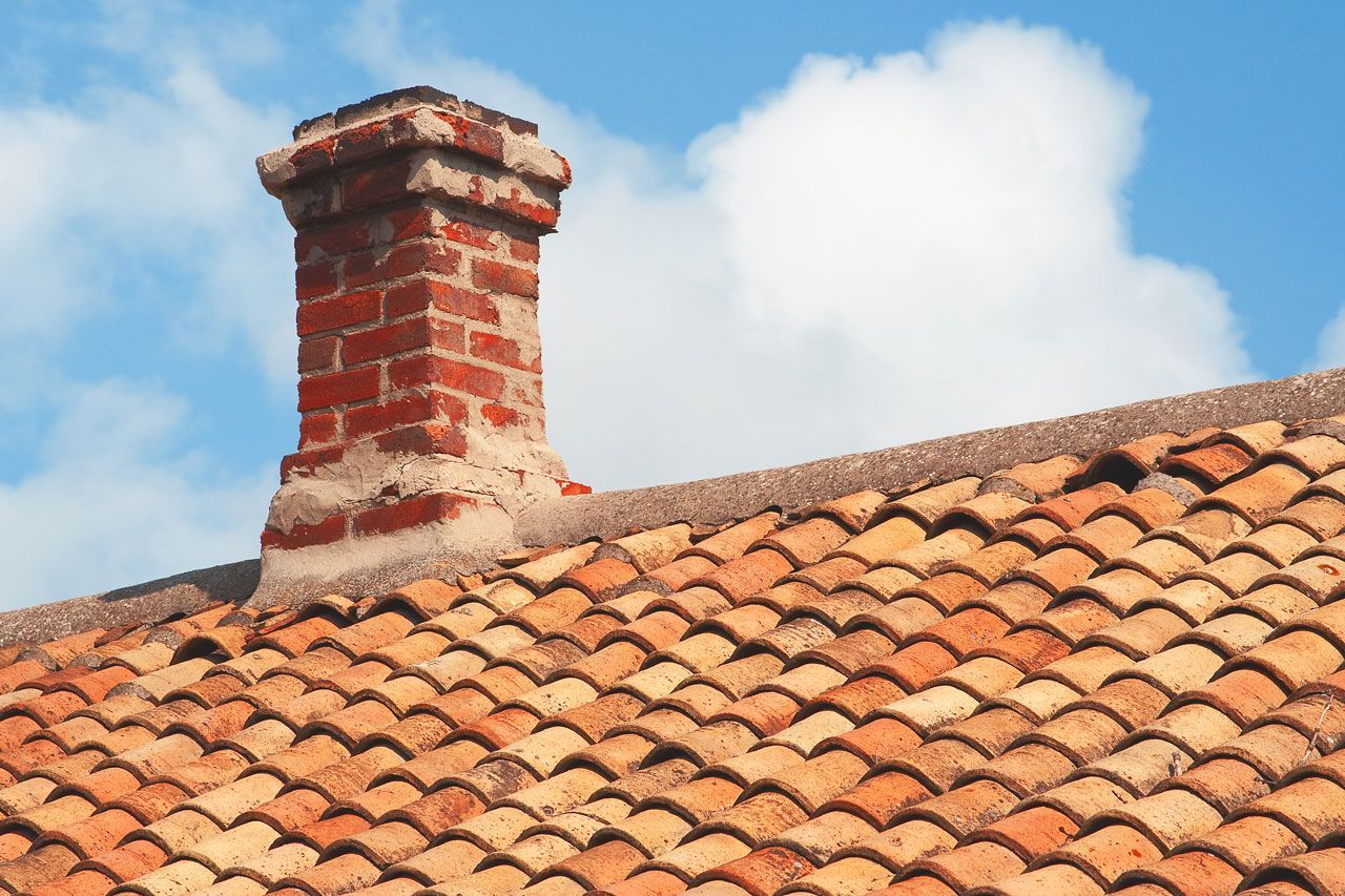 Brick chimney on a tiled roof against a blue sky with clouds.