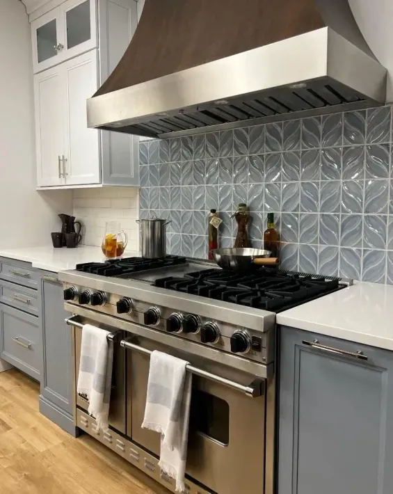 Modern kitchen with stainless steel range, hood, blue-gray cabinets, and patterned tile backsplash by American Home Remodeling