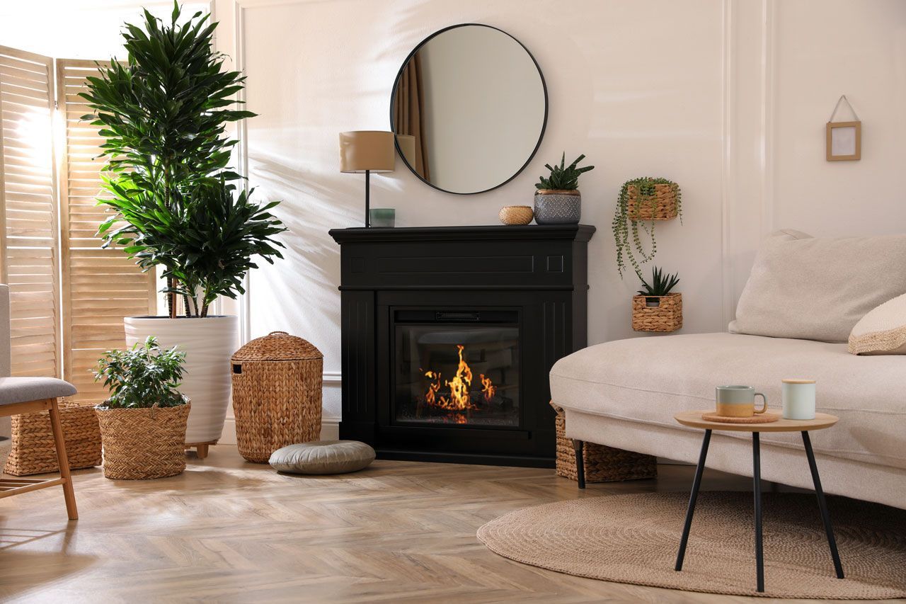 Living room with black fireplace, round mirror, plants, and beige sofa.