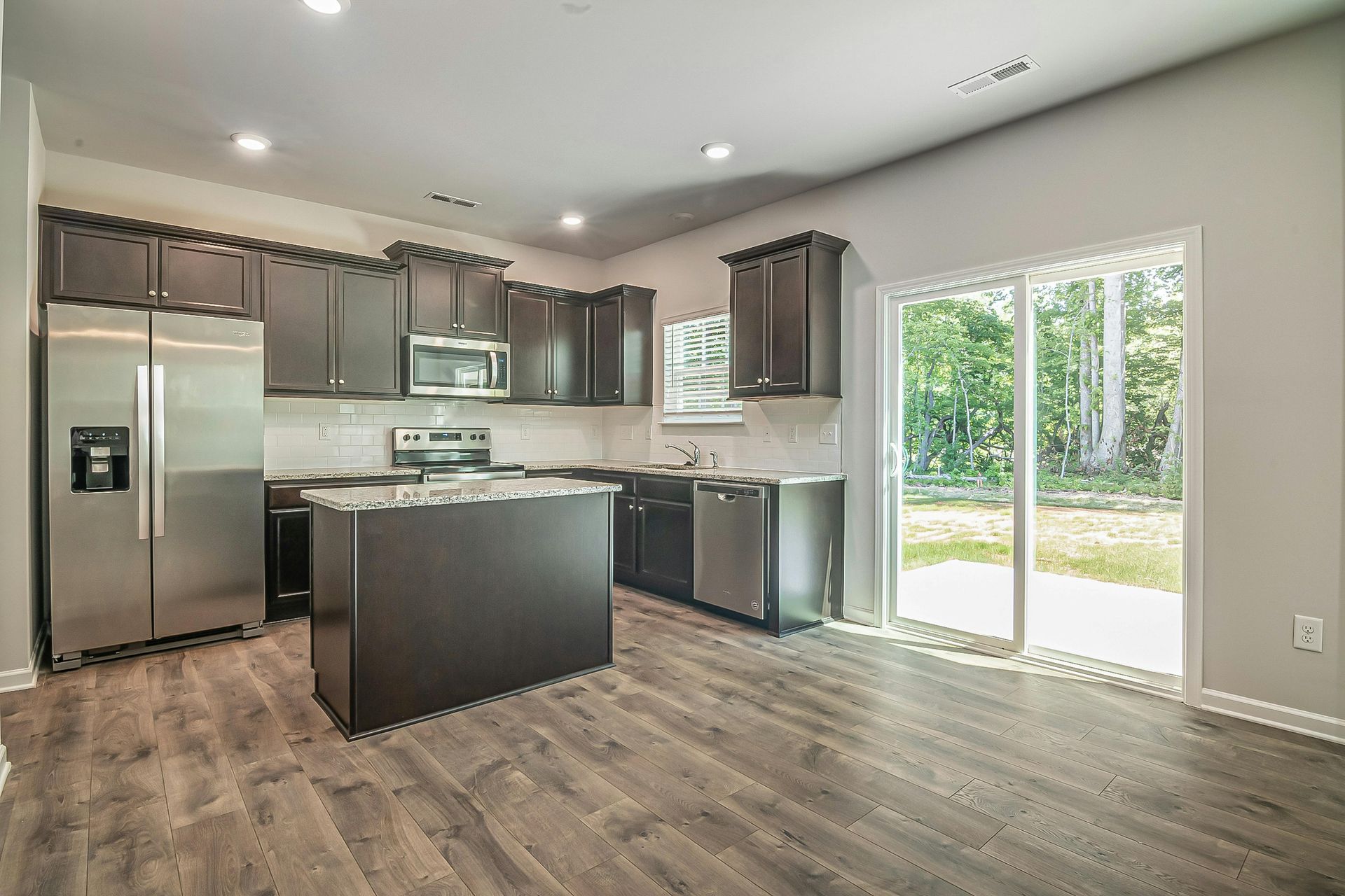 Modern kitchen with dark cabinetry, stainless steel appliances, and sliding glass door.
