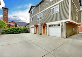 Multi-story townhouse with concrete driveway, garage doors, and a brick tower in the background.