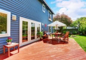 Blue house with a wooden deck, patio furniture, and a striped umbrella in the backyard.