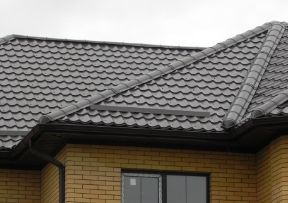 Grey metal roof on a brick building with a dark gutter and a window.