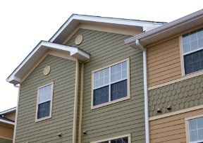 Multi-story apartment building with green and tan siding, white trim, and windows.