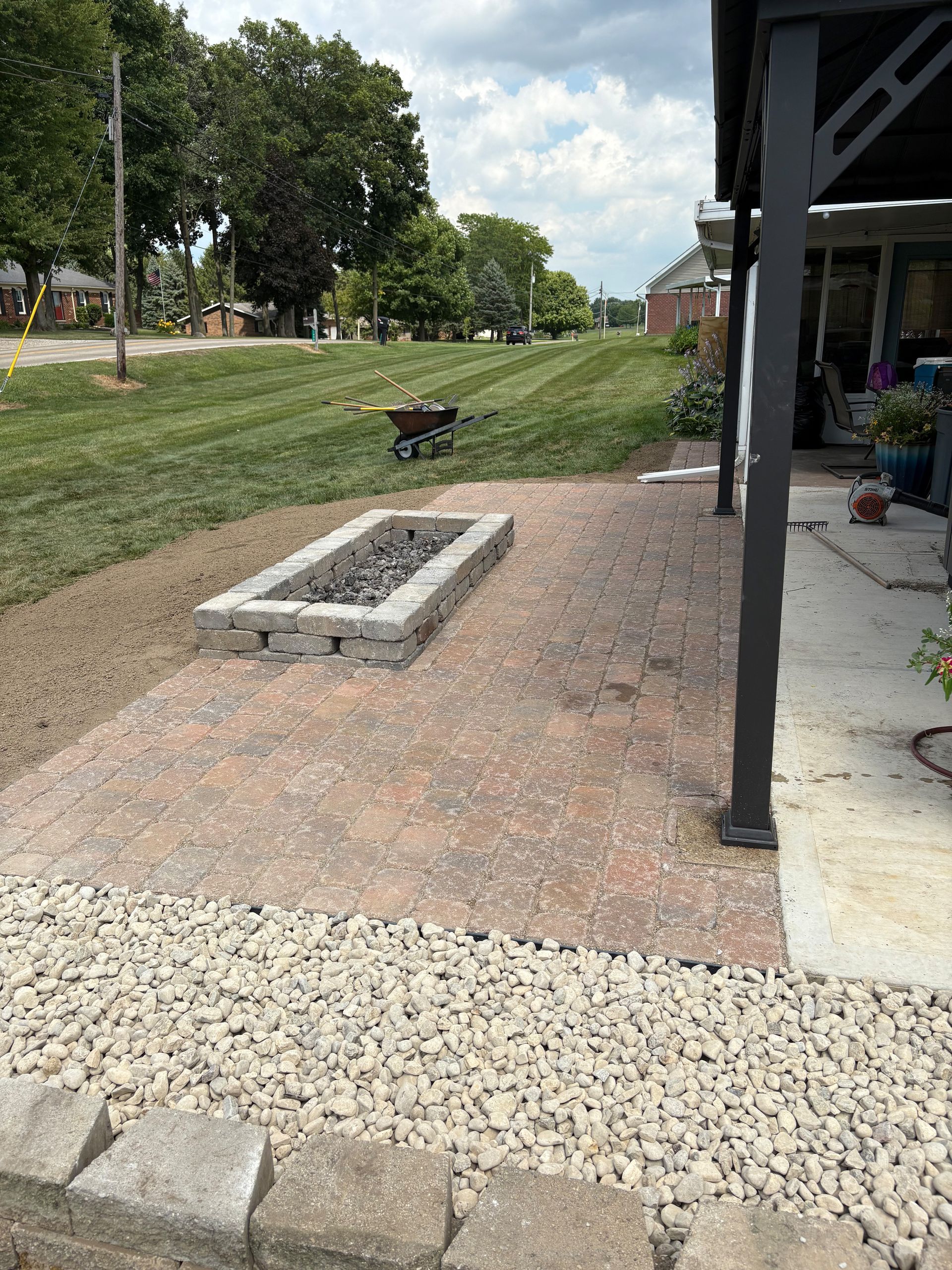 Backyard patio with a fire pit and gravel border near a grassy lawn and house.